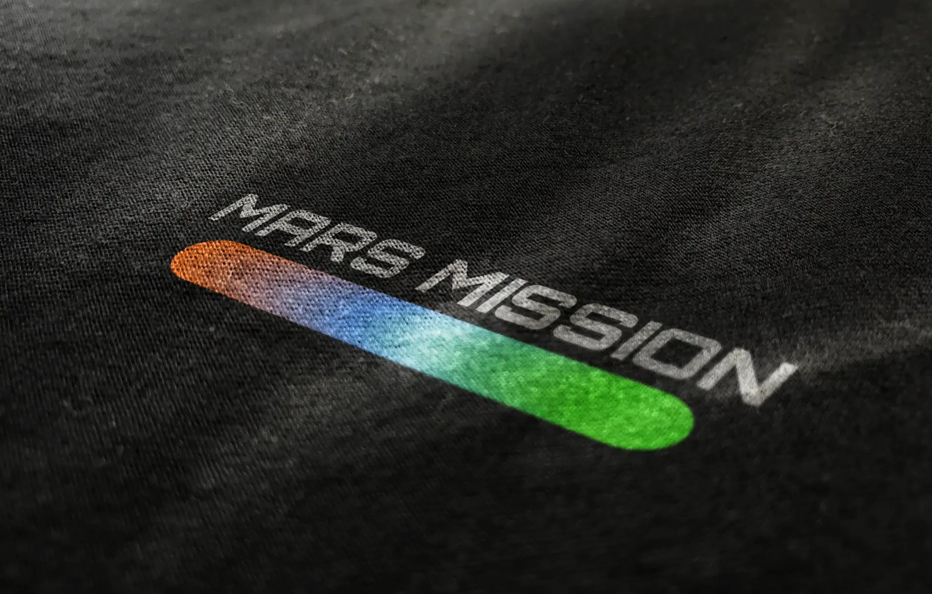 Close-up of Mars Mission logo with red-to-green gradient bar symbolizing three phases of Mars transformation, printed on black fabric.