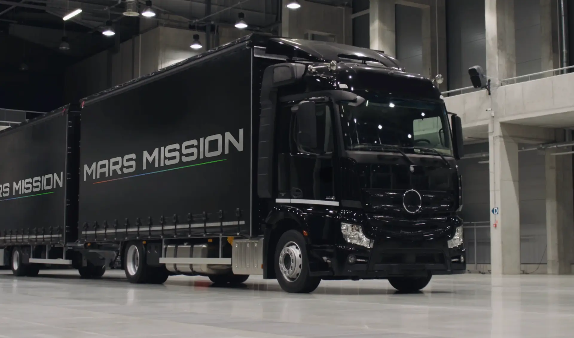 Black transport truck with Mars Mission branding and gradient line representing three phases of Mars transformation, parked in industrial facility.