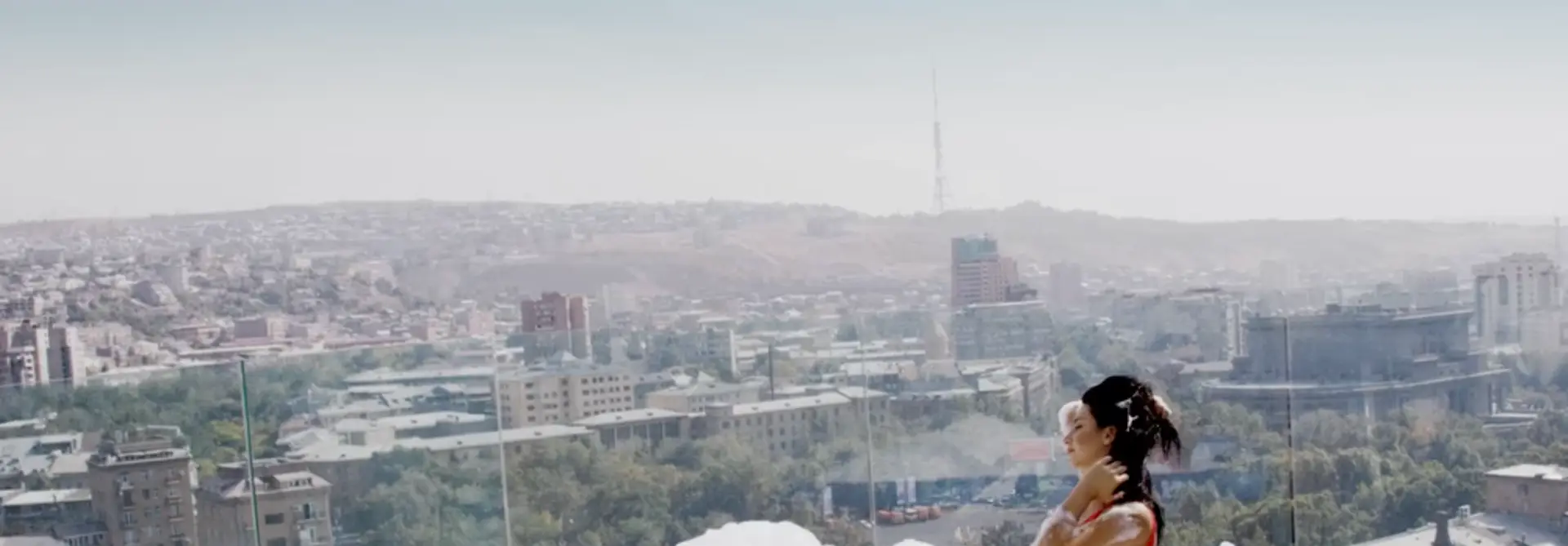 Woman relaxing in rooftop pool overlooking Yerevan cityscape with panoramic view and television tower in the distance.